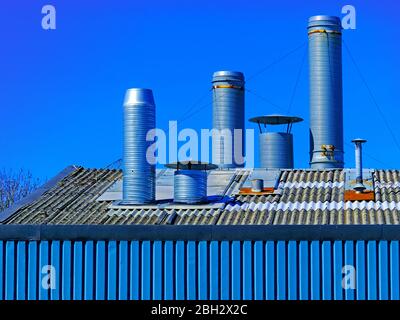 Set di 3 grandi condotti di ventilazione sopra il tetto della fabbrica contro il cielo blu intenso Foto Stock