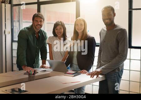 Quattro simpati colleghi che si trovano in un ufficio moderno sorridendo alla macchina fotografica Foto Stock