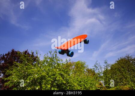 Uno skateboard rosso che si innalcia, gainst un cielo blu perfetto e alberi verdi Foto Stock