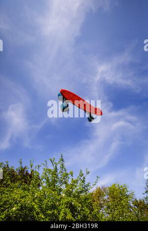 Uno skateboard rosso che si innalcia, gainst un cielo blu perfetto e alberi verdi Foto Stock