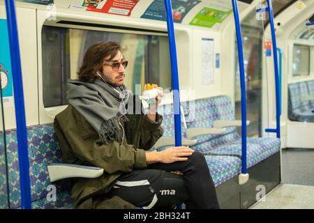 Ritratto di un giovane seduto in occhiali da sole e mangiare un hamburger sulla metropolitana di Londra Foto Stock