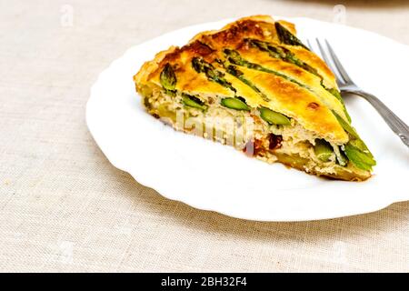 Fetta di crostata tagliata con asparagi verdi e formaggio tostato in tavola Foto Stock