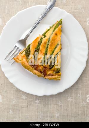 Fetta di crostata tagliata con asparagi verdi e formaggio tostato in tavola Foto Stock