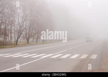 Nebbia fitta e nebbia fitta e attraversata in strada con traffico, pericolo sulla strada, nebbia autunnale Foto Stock