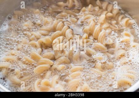 Pasta a grani interi in una padella con acqua bollente e un cucchiaio. Cucinare cibo sano Foto Stock