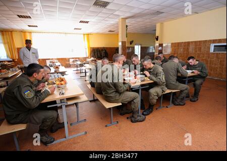 In corrispondenza di un pasticcio hall: soldati seduti al set-tabelle e mangiare. Novo-Petrivtsi base militare, Ucraina. Novembre 12, 2018 Foto Stock