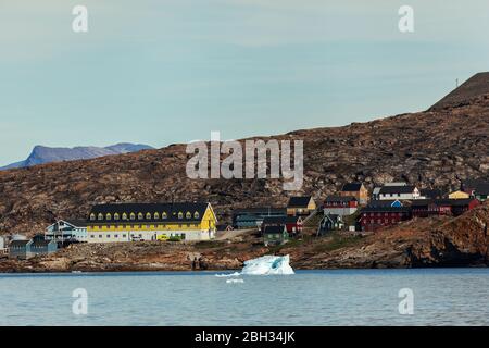 Case tradizionali nella baia di Upernavik con un grande edificio pubblico giallo, con iceberg in prima linea Foto Stock