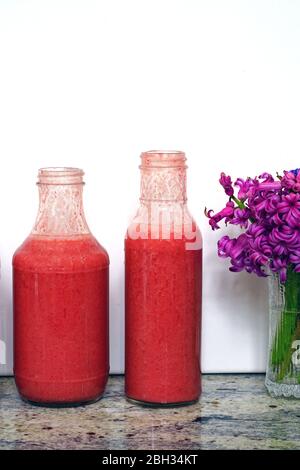 Bottiglie di vetro riempite con frullati di fragole freschi e colorati fatti in casa Foto Stock