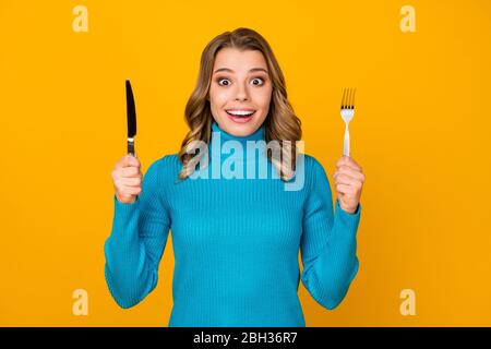 Foto di affascinante ragazza ondeggiante tenere in metallo coltello forchetta pronto per iniziare gustoso cibo cena pasto buon appetito indossare blu dolcevita isolato luminoso Foto Stock