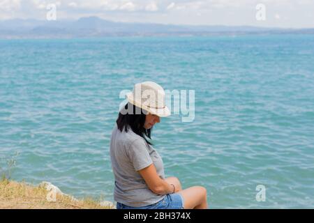 Bella donna lifestyle seduta e rilassante sulla riva del lago contemplando un paesaggio incredibile. Vacanza estiva in famiglia. Rilassatevi. Felicità Foto Stock