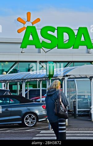 Una vista sulla strada del superstore Asda a Bridgend. Donna che attraversa la strada per conservare strada coperta. Foto Stock