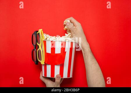 Il tipo tiene il popcorn nelle sue mani su uno sfondo rosso. Inserire il testo. Foto Stock