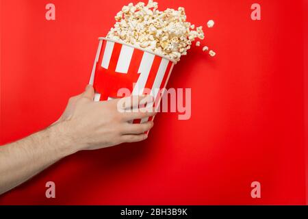 Il tipo tiene il popcorn nelle sue mani su uno sfondo rosso. Inserire il testo. Foto Stock