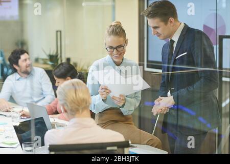 Giovane coppia di lavoro che legge i documenti insieme e li discute durante un incontro d'affari all'ufficio Foto Stock