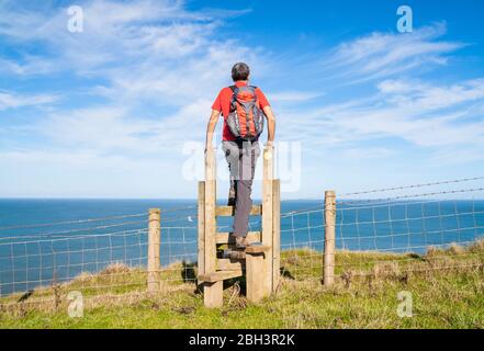 Maschio escursionista che attraversa Stille sul sentiero nazionale Cleveland Way tra Skinningrove e Staithes, North Yorkshire, Inghilterra, Regno Unito Foto Stock