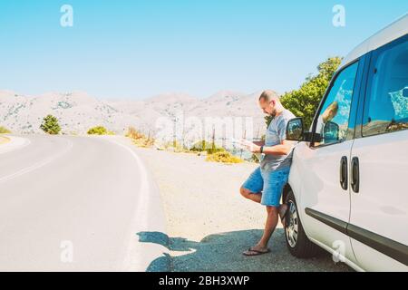 Un uomo con una mappa della zona vicino alla macchina è in piedi sulla strada. Concetto di auto viaggio. Foto Stock