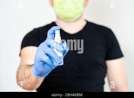 Uomo con guanti chirurgici e maschera facciale che si protegge dalla trasmissione di malattie e covid-19 con e disinfettante spray per le mani. Foto Stock