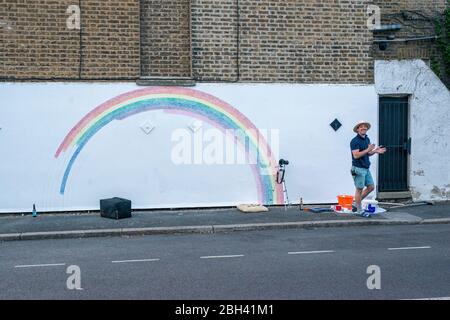 Camberwell, Londra, Regno Unito. 23 aprile 2020. Louis Young e vicini si applaudiono per il NHS il giovedì sera accanto a un murale di un arcobaleno sul muro della sua casa per ringraziare il NHS. Foto Stock