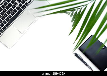 Vista dall'alto della scrivania bianca per ufficio con computer portatile, notebook, foglia di palma e accessori. Lavorare da casa concetto. Vista dall'alto con spazio per le copie. Primo piano. Foto Stock