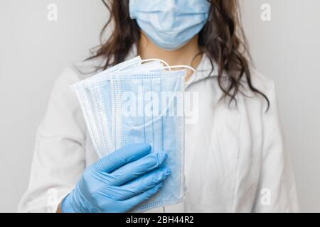 Arrestare SARSCoV, virus 2020, COVID-19. Le mani di Womans nei guanti medici blu che tengono una maschera protettiva. Medico che indossa la maschera facciale di protezione contro Foto Stock