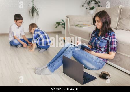 Rimani a casa, mamma che lavora in remoto su un notebook nel soggiorno mentre i bambini giocano. Compiti a casa. Concetto di distanza sociale. Quarantena. Chiudi, Foto Stock