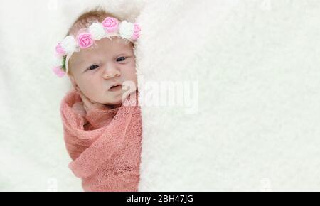 Divertente bambina neonato in un pannolino rosa e una corona di fiori sulla testa. Spazio di copia Foto Stock