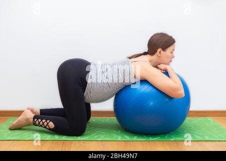 Esercizi di palla di Biding durante il concetto di gravidanza. Giovane donna incinta caucasica che pratica sulla sfera di idoneità Foto Stock