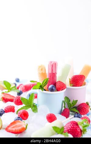 Papicle di frutta intera sane con fragole di Berries Kiwi su sfondo chiaro con un decor di ghiaccio, menta. Gustoso gelato alla frutta nella tazza. Spazio di copia. Foto Stock