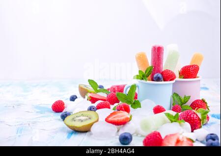 Papicle di frutta intera sane con fragole di Berries Kiwi su sfondo chiaro con un decor di ghiaccio, menta. Gustoso gelato alla frutta nella tazza. Spazio di copia. Foto Stock