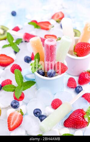 Papicle di frutta intera sane con fragole di Berries Kiwi su sfondo chiaro con un decor di ghiaccio, menta. Gustoso gelato alla frutta nella tazza. Spazio di copia. Foto Stock