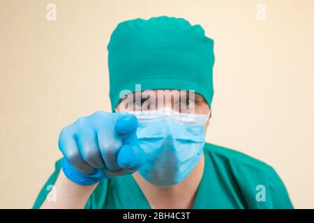 Il medico che indossa guanti protettivi verdi blu e maschera facciale blu punta dritto avanti. Foto Stock