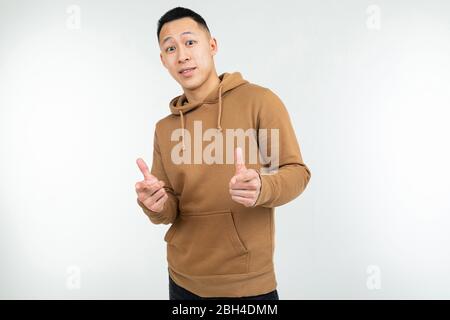 un uomo asiatico sicuro con felpa con cappuccio marrone mostra le mani come su sfondo bianco. Foto Stock