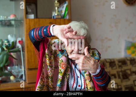 Una donna anziana in abiti luminosi mostra con le mani gesto foto cornice. Foto Stock