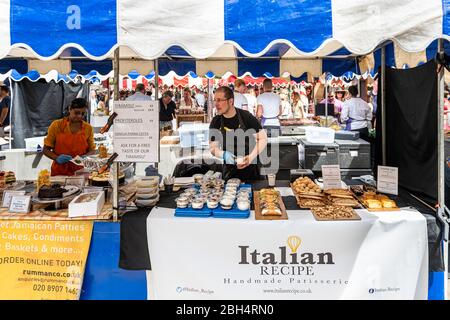 Londra, UK - 23 giugno 2018: Persone al chiosco di vendita di cibo in strada mercato weekend a Chelsea durante la giornata estiva di sole con ristorante italiano panetteria Foto Stock