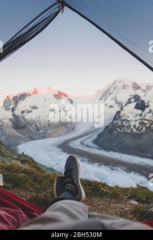 Uomo sdraiato all'interno della tenda con il Ghiacciaio Gorner in lontananza in Vallese, Svizzera Foto Stock