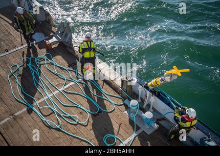 23 aprile 2020, Schleswig-Holstein, Helgoland: I lavoratori preparano la corda per una tonnellata. Segnale di partenza per un grande campo di test marittimo al largo di Helgoland: Gli scienziati del Centro di test per le tecnologie marittime hanno utilizzato tonnellate per contrassegnare un'area di tre milioni di metri quadrati non lontano dall'isola del Mare del Nord. Esso è destinato a fornire in futuro impianti di prova per la robotica marittima. Produttori e scienziati possono testare diversi scenari. Ad esempio, i veicoli subacquei autonomi per turbine eoliche offshore possono essere testati in condizioni reali in mare o droni che volano sull'acqua per Foto Stock