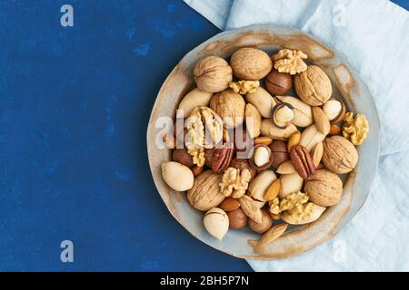 Blu classico nel cibo. Mix di noci sul piatto - noce, mandorle, noci pecan, macadamia Foto Stock