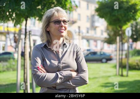 Ritratto di maturo business donna fiduciosa con braccia ripiegate, femmina con occhiali camicia in città Foto Stock