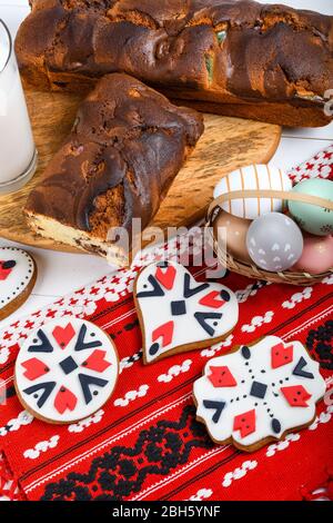 Fette di pan di Spagna rumeno con asciugamano tradizionale rosso con punto manuale su asse di legno, uova dipinte di Pasqua e zenzero fatto in casa cuori, UN Foto Stock