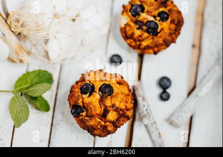 Muffin sani con farina di cocco e mirtilli su piatto di legno chiaro decorato con conchiglie di menta e conchiglia Foto Stock