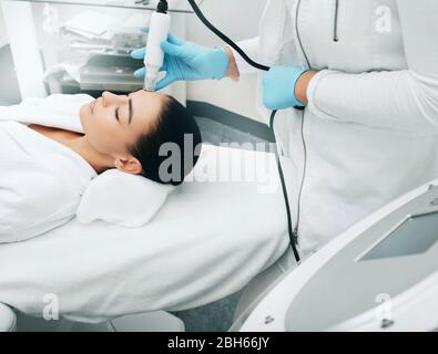 Beautician con macchina no-aghi mesoterapia leviga le rughe della pelle della fronte femminile . Metodo di ringiovanimento della pelle indolore Foto Stock