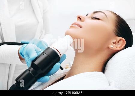 Beautician che fa una terapia di onda acustica ad una donna. Ringiovanimento della pelle con onde acustiche, faccia ravvicinata Foto Stock