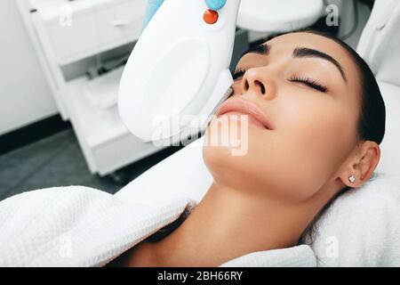 Donna brunetta durante rimuove macchie marroni sul viso, Beautician utilizzando la tecnologia di ringiovanimento ELOS Foto Stock