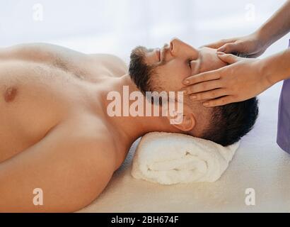 Uomo affascinante che si rilassa con gli occhi chiusi durante il massaggio alla testa presso il centro benessere. trattamento antidolorifico per la testa con massaggio Foto Stock