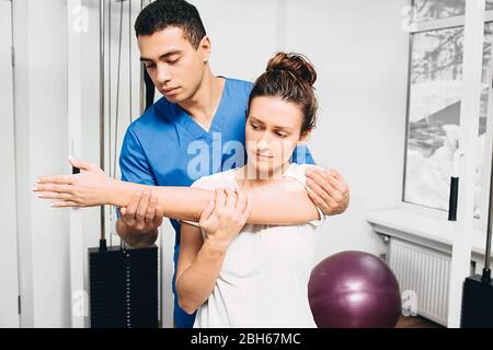 Donna con lesioni al giunto a gomito. Dolore articolare. Fisioterapista tiene la mano di una donna durante la riabilitazione Foto Stock