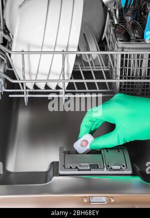 Primo piano una compressa con detergente in mano di una donna sullo sfondo della lavastoviglie Foto Stock