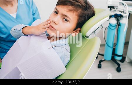 ragazzo con denti soffrire seduto su sedia dentale. mal di denti, bambino tristemente guardando la macchina fotografica Foto Stock