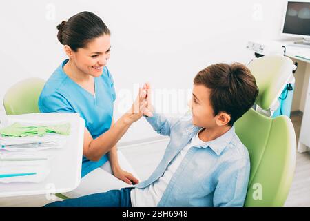 Felice ragazzino che ha cinque con il suo dentista . Si siede su sedia dentale, dopo il trattamento dei denti. Odontoiatria pediatrica Foto Stock