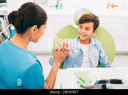 Sì, i denti trattati sono freddi e non spaventosi. Felice ragazzino che ha cinque con il suo dentista . Si siede su sedia dentale, dopo il trattamento dei denti. Foto Stock