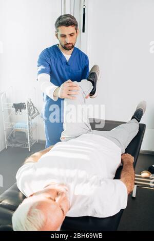 fisioterapista trattamento lesioni alle gambe su un uomo sdraiato. Uomo anziano che si allena con il suo terapeuta. Trattamento del dolore alle articolazioni, al ginocchio e alle gambe Foto Stock